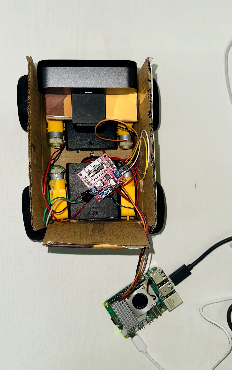 Top-down view inside Boxtron's cardboard chassis: motors, motor driver board, battery pack, and the Raspberry Pi 5 wired underneath